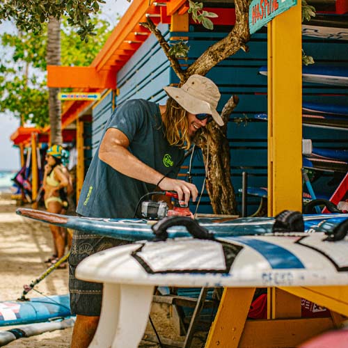 Man sanding surfboard in beach hut