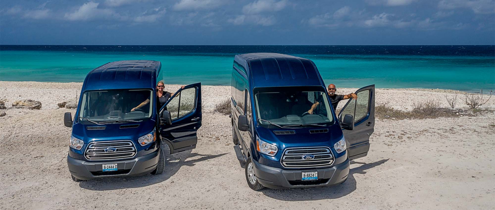 Two blue vans with drivers parked by the ocean