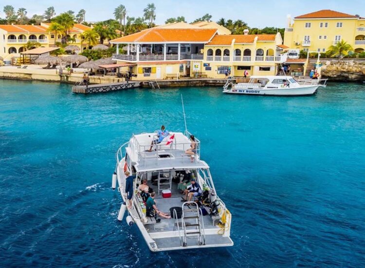 People aboard a large boat in the ocean with buildings in the background