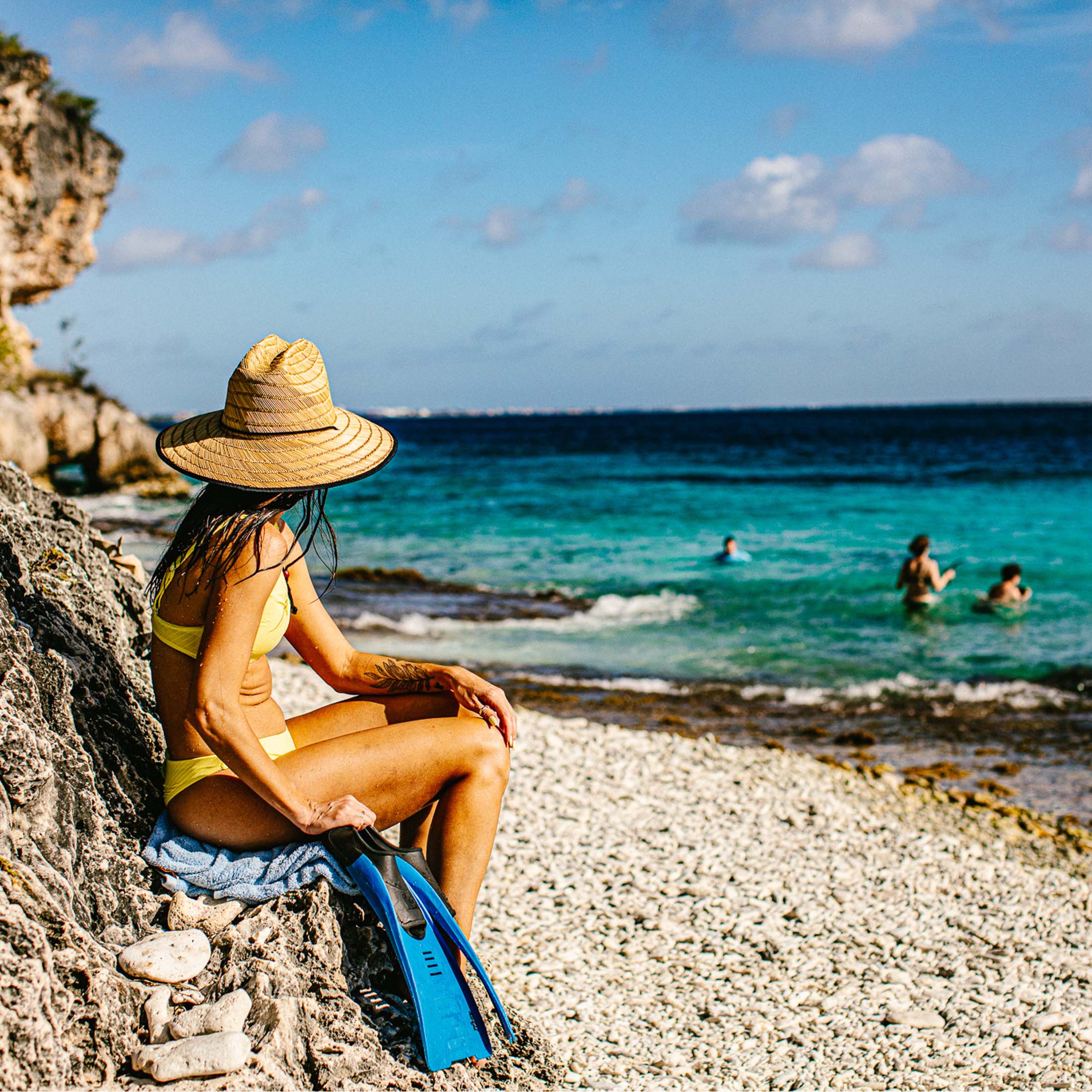 Woman enjoying a tropical breeze while sitting on a rocky cliff overlooking the Caribbean Sea.