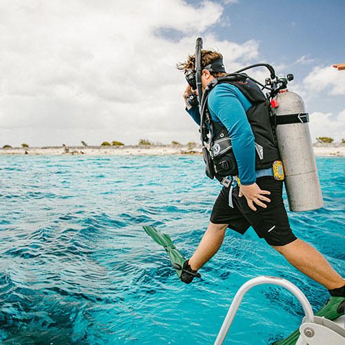 Man jumping into the water wearing scuba diving gear in bonaire