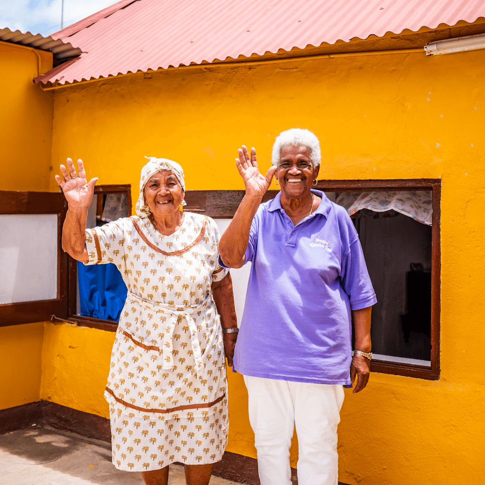 Two women standing in front of building outside, smiling and waving to camera